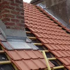 Dachdecker arbeiten am Kamin, um ihn einbleien. Neue rote Dachziegel werden verlegt.