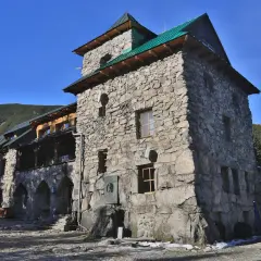 Kamienny budynek schroniska w Tatrach Polskich, z zielonym dachem i widokiem na górzyste tereny.