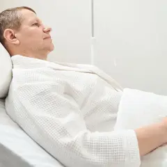 Mężczyzna w białym szlafroku leży w łóżku szpitalnym, przechodząc rekonwalescencję po usunięciu pęcherza moczowego.