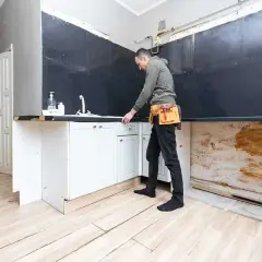 Remont kuchni od czego zacząć? Mężczyzna w pasie narzędziowym sprawdza szafki pod zlewem.
