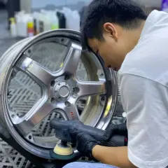 Mężczyzna w czarnych rękawiczkach poleruje felgę aluminiową, przywracając jej blask.