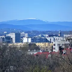 Widok na nowoczesne budynki Krakowa z oddali, na horyzoncie majaczy ośnieżona Babia Góra z Krakowa.
