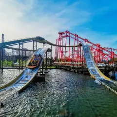 Energylandia Zator atrakcje: łodzie z pasażerami zjeżdżają po stromych zjeżdżalniach wodnych, w tle czerwone rollercoastery.