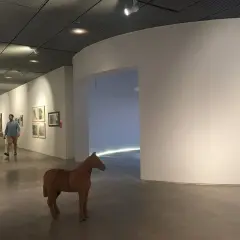 Un hombre pasea por una sala de exposiciones, admirando las obras de arte y una escultura de caballo. Una visita a los museos de Lugo.