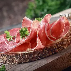 Kanapka z ciemnego pieczywa obficie posypanego ziarnami, z plasterkami aromatycznego salami i natką pietruszki.