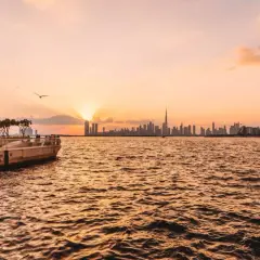 Sonnenuntergang über Dubai. Die Skyline mit dem Burj Khalifa und Palmen am Ufer sind einige der Dubai Highlights.