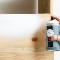 Mano aplica imprimación en spray a madera. Es necesario imprimar antes de pintar madera para un acabado perfecto.