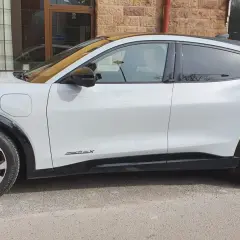 Vit Ford Mustang Mach-E står parkerad utanför en tegelbyggnad. En cykel syns i bakgrunden. Detta är en ford mustang mach-e test.