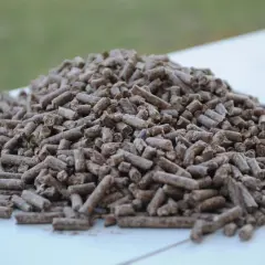 Góra drobnych, brązowych pelletów, idealnych jako dodatek do pelletu, leży na białej powierzchni.