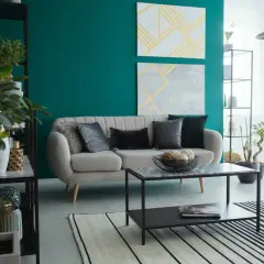 Nowoczesny salon z kanapą i fotelem w kolorze butelkowej zieleni. Dodatki, takie jak poduszki i rośliny, podkreślają ten głęboki odcień.