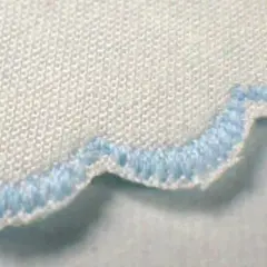Close-up of a white fabric with a scalloped edge finished with light blue stitching. This decorative edge is called a picot.