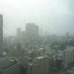 Regen prasselt auf ein Fenster mit Blick auf eine Stadt in Japan. Die Sicht ist durch die Tropfen und den grauen Himmel getrübt, typisch für die japan taifun saison.