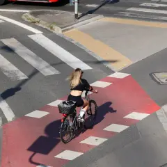 Kobieta na rowerze przejeżdża przez czerwony pas rowerowy, zbliżając się do **uwaga przejście dla pieszych**.