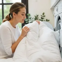 A woman is placing a white duvet into a washing machine, demonstrating how to wash duvet cover.