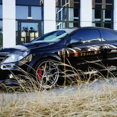 Czarny Opel Astra GTC z chromowanymi felgami i czerwonymi zaciskami hamulcowymi, zaparkowany przed nowoczesnym budynkiem, otoczony suchą trawą.