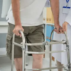 Un uomo anziano, con una sensazione di camminare storto, si appoggia a un deambulatore mentre un medico lo assiste.