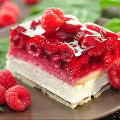 Szybkie ciasto z malinami mrożonymi, z galaretką i bitą śmietaną, ozdobione świeżymi malinami i miętą.