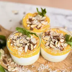 Drei Gläser mit cremigem Kokos Dessert vegan, garniert mit Mango-Püree, Mandelblättchen und Kokosraspeln.