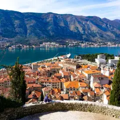 Widok na kotor stare miasto z czerwonymi dachami, zatokę i góry w tle.