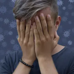 Nastolatek zakrywa twarz dłońmi na tle wirusów.