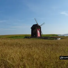 Wiatrak z czerwoną wstęgą na tle pól i falujących paneli słonecznych w Sierakowskim Parku Krajobrazowym.