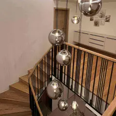 Nowoczesne lampy na klatkę schodową w kształcie kul, wiszące nad drewnianymi stopniami i czarną balustradą.