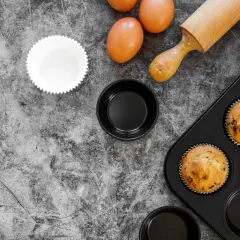 Gotowe muffinki w foremkach do ciast, jajka i wałek do ciasta na kamiennym blacie.