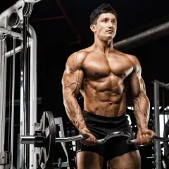 Mężczyzna z wyrzeźbionym ciałem wykonuje ćwiczenia na biceps z łamaną sztangą w siłowni.