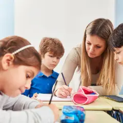 Lehrerin hilft Kindern in der Schule beim Schreiben.