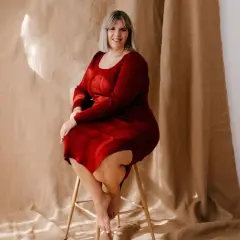 Uśmiechnięta kobieta w czerwonej sukience dresowej plus size siedzi na stołku.