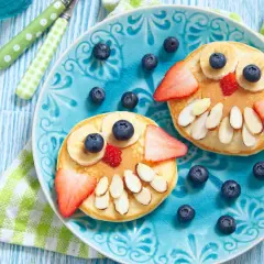 Due pancake a forma di gufo, decorati con frutta e mandorle, per una colazione sana bambini.