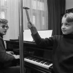 Zbigniew Wodecki gra na pianinie, a Paweł Wodecki trzyma młotek, jakby chciał uderzyć w klawisze.