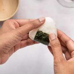 Hands shaping a perfectly sized onigiri, a delicious rice ball wrapped in nori seaweed.