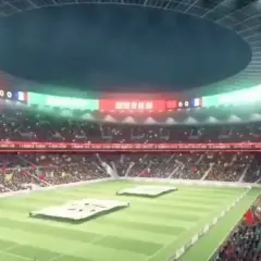 Widok na trybuny wypełnione kibicami na największym stadionie na świecie. Na murawie rozłożone są dwa białe transparenty.