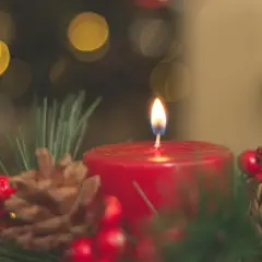 Ein Adventskranz mit brennender Kerze, Tannenzweigen, Zapfen und Beeren. Die Bedeutung des Adventskranzes liegt in der Vorfreude auf Weihnachten.