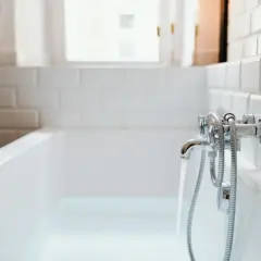 Wanna z wodą, woda leje się z kranu. Trwa wymiana syfonu w wannie zabudowanej.