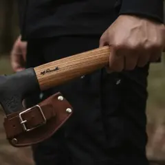 Mano sujetando hachas tácticas con funda de cuero. El mango de madera tiene una inscripción.