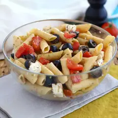 En härlig italiensk pastasallad med penne, tomater, svarta oliver och fetaost i en glasskål. Perfekt för en lätt lunch.