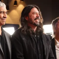 Trzech członków Foo Fighters: Nate Mendel, Dave Grohl i Chris Shiflett, uśmiechają się i patrzą w bok.