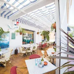Terraza de restaurante con mesas y sillas, toldos a rayas y vegetación. Un cartel anuncia "il brigantino san jose".