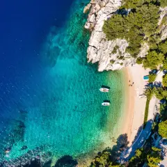 Idealny pole namiotowe Chorwacja: piaszczysta plaża, turkusowa woda, łodzie kołyszące się na falach, otoczone zielenią i skałami. Raj dla wypoczynku.