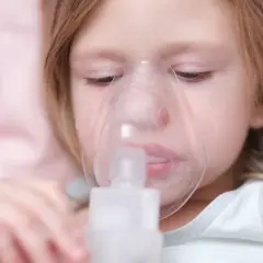 Mała dziewczynka z maską inhalacyjną na twarzy. Inhalacja nawilżająca gardło przynosi ulgę.