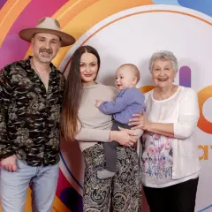 Mateusz Ziółko z rodziną: żoną, synkiem i mamą na tle kolorowego logo.