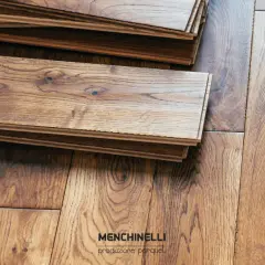 Pezzi di parquet in legno di rovere impilati, pronti per la finitura. La venatura naturale del legno è ben visibile.