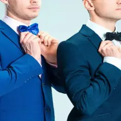Dwóch mężczyzn w eleganckich garniturach, jeden w niebieskim, drugi w granatowym, poprawia muszki. Jaka mucha do granatowego garnituru?