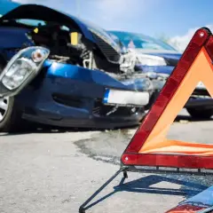 Triangolo di emergenza davanti a due auto danneggiate dopo un incidente. Un poliziotto documenta i danni, forse un incidente senza assicurazione.