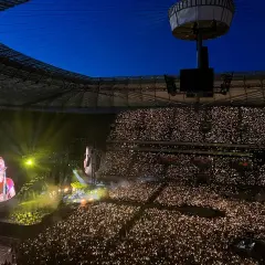 Koncert na stadionie, tłum z zapalonymi telefonami, na ekranie wokalista Coldplay.