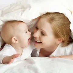 Mutter und ihr **baby 5 wochen** alt kuscheln unter einer Decke und lachen sich an.