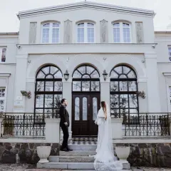 Para młoda przed Lisewskim Dworem. Elegancka biel sukni ślubnej i czarny garnitur pana młodego kontrastują z fasadą zabytkowego budynku.