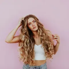 Kobieta z falowanymi blond włosami, które wyglądają na zdrowe i lśniące, jakby użyła dobrego kremu na włosy.